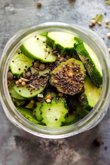 pickling spices on sliced cucumbers in jar