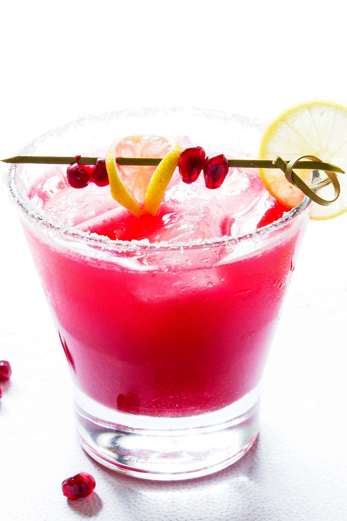 bright pink pomegranate margarita in short glass with pomegranate and lime slice decoration