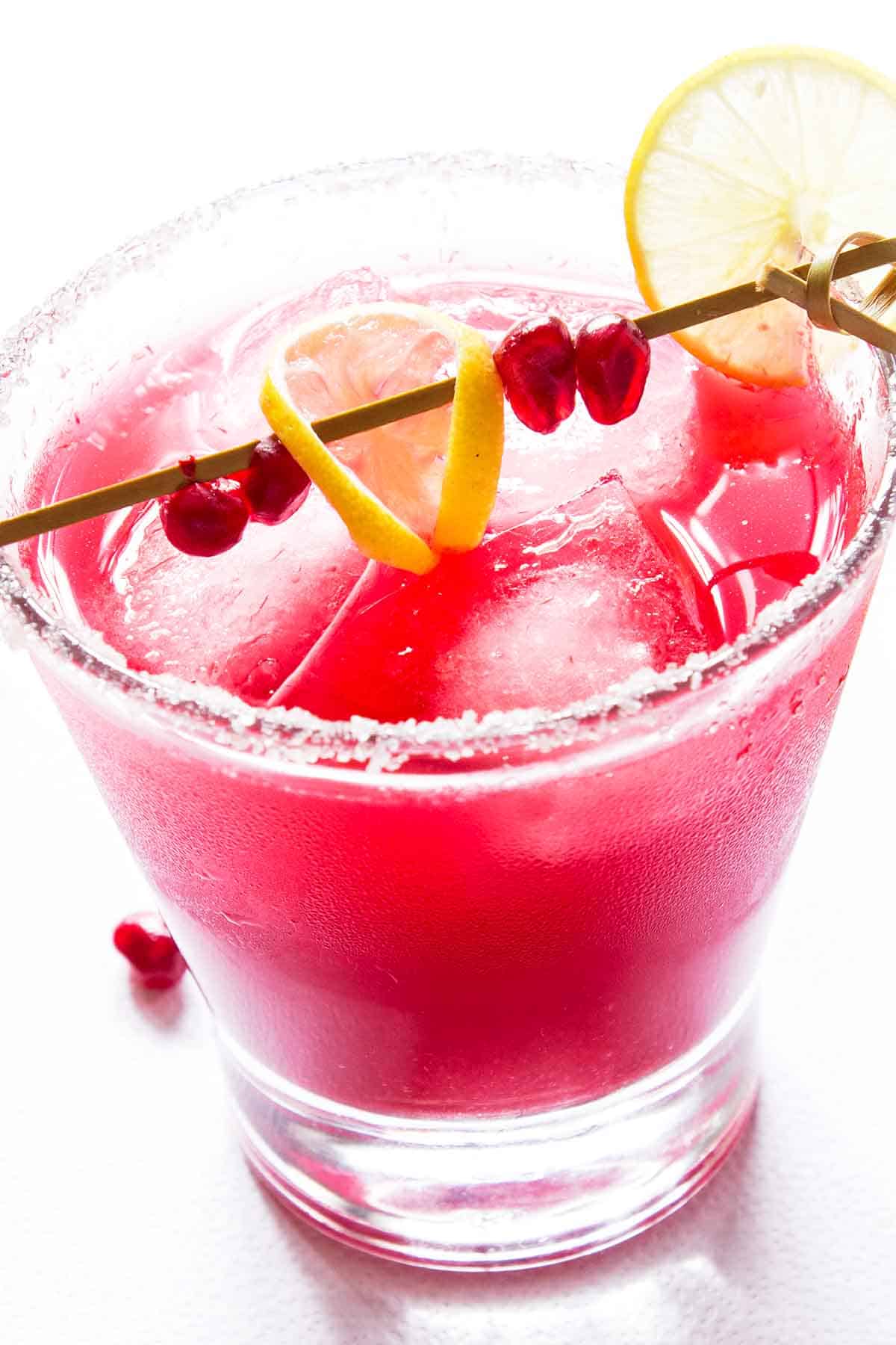 Deep pink pomegranate margarita in glass with lemon slice and stir stick