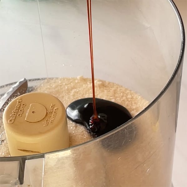 molasses pouring onto granulated sugar in food processor