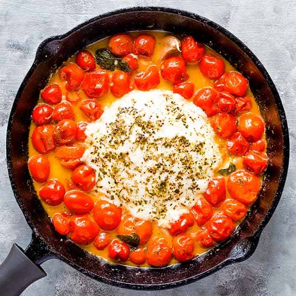 melted cheese circle and burst cherry tomatoes in black pan