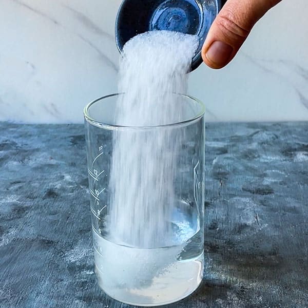 hand adding salt to water in glass