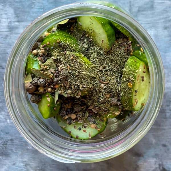 mason jar with cucumber slices, pickling spice, and dill