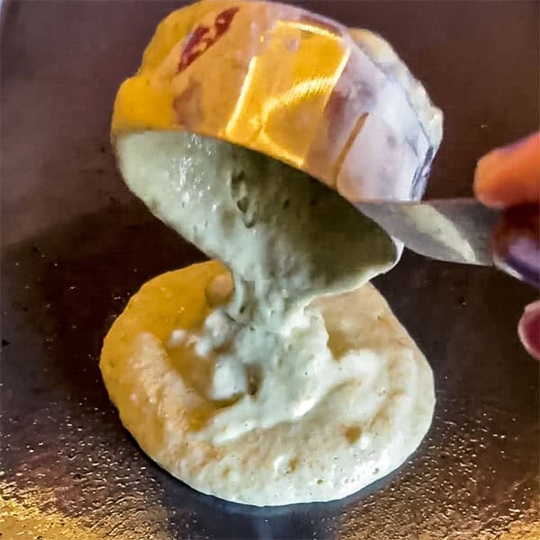 measuring cup dropping pancake batter onto griddle