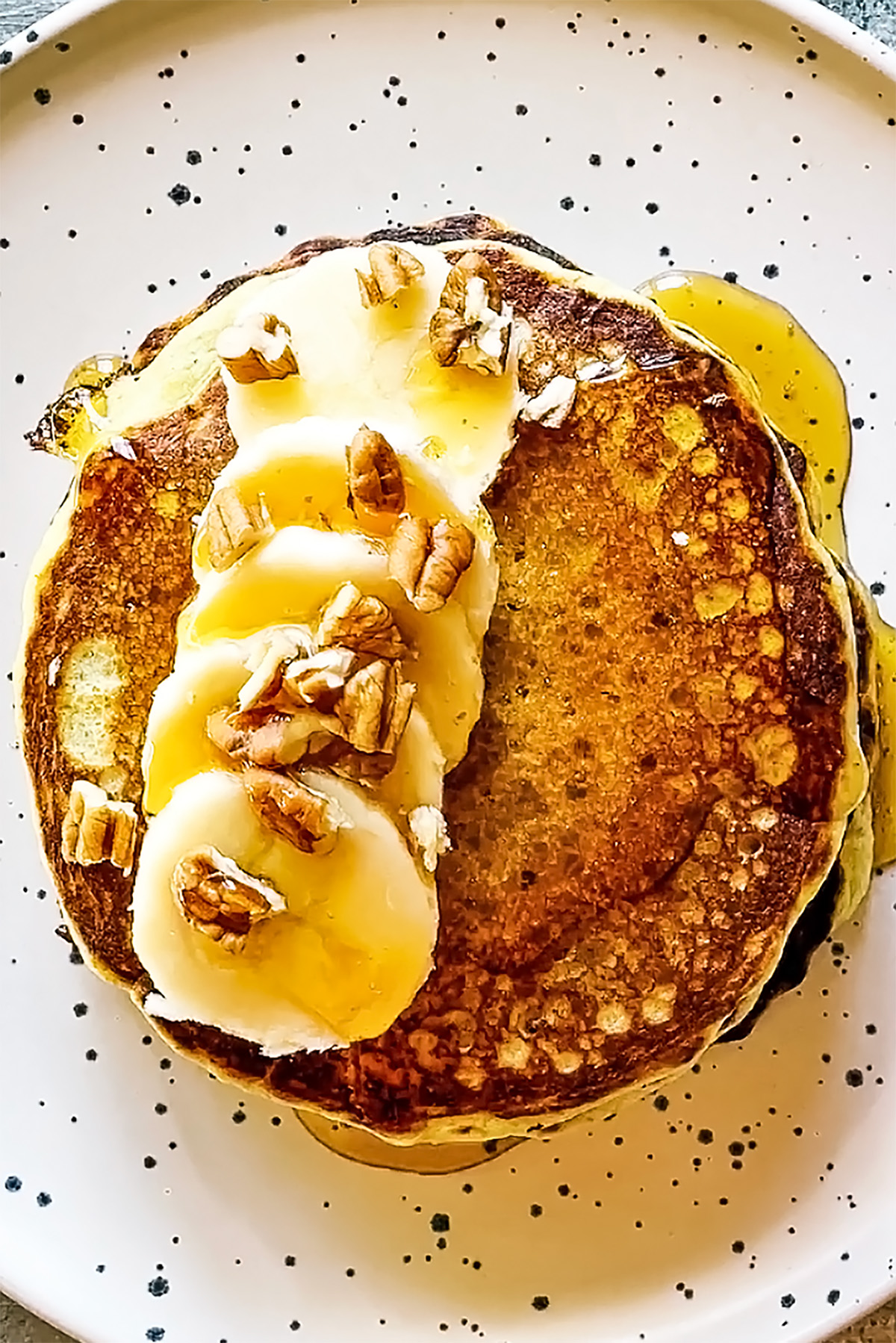 stack of protein powder pancakes topped with banana slices, pecans, and maple syrup