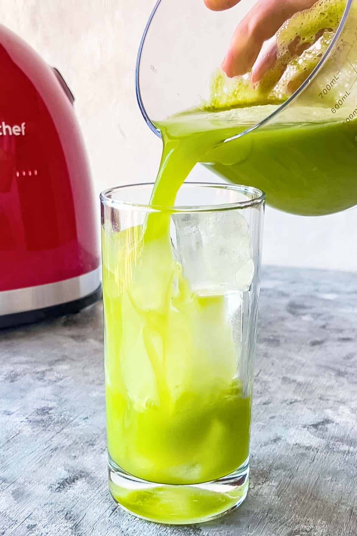 green apple cucumber juice pouring into glass with ice